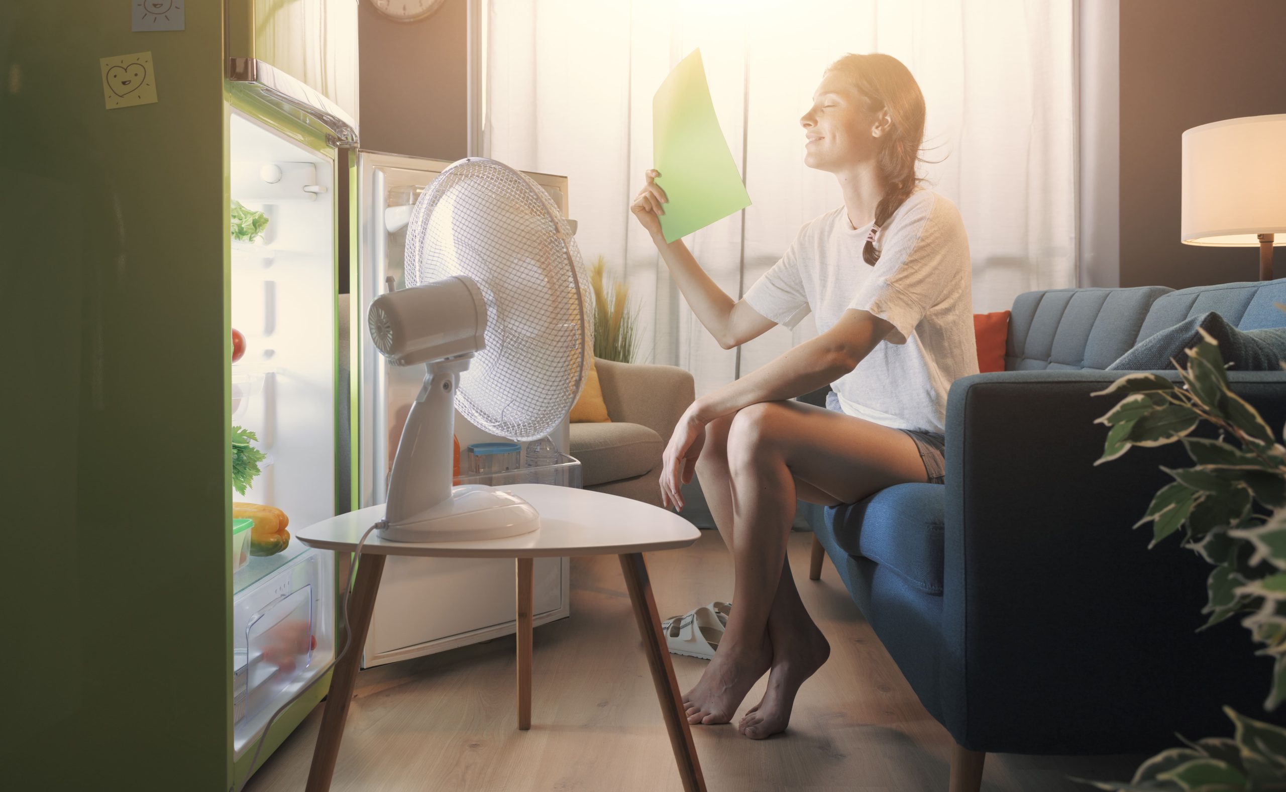 Woman trying to cool off during summer heat by sitting in front of the fridge with a fan going